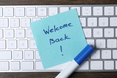Photo of Paper note with phrase Welcome Back, marker and keyboard on table, top view