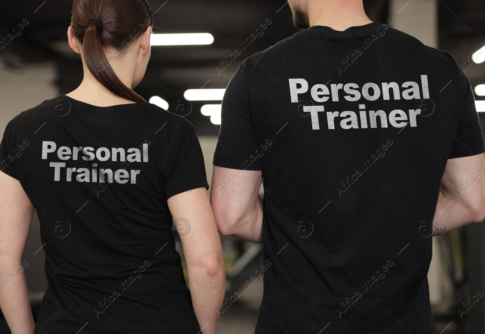 Personal trainers wearing t-shirts with inscriptions in gym, closeup. Back view Image of Personal trainers wearing t-shirts with inscriptions in gym, closeup. Back view