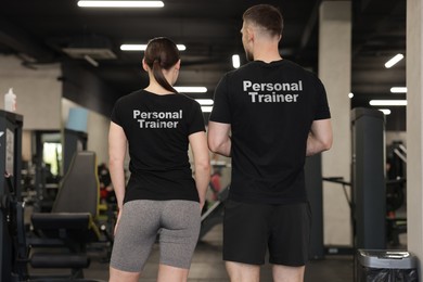 Image of Personal trainers wearing t-shirts with inscriptions in gym. Back view