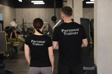 Image of Personal trainers wearing t-shirts with inscriptions in gym. Back view