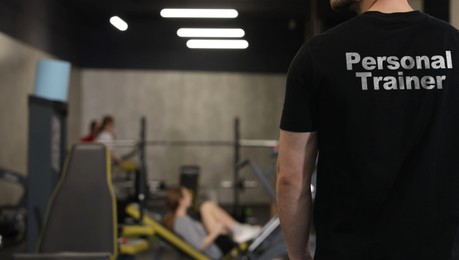 Image of Personal trainer wearing t-shirt with inscription in gym, closeup. Back view