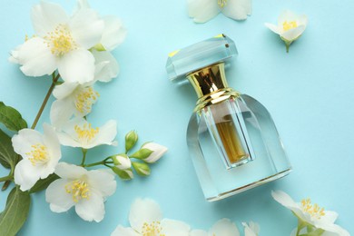 Photo of Bottle of perfume and beautiful jasmine flowers on light blue background, flat lay