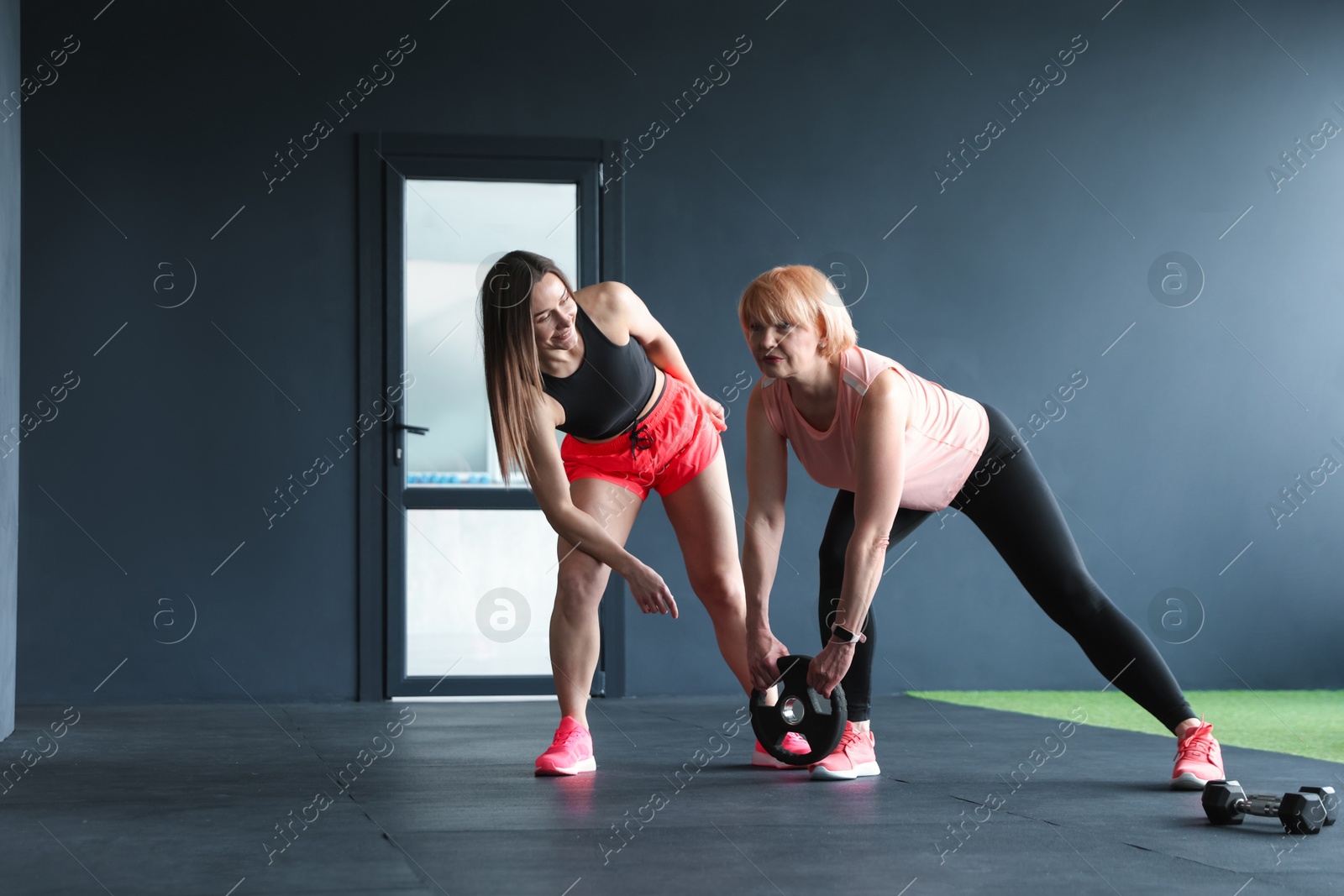 Senior woman training with weight plate supervised by professional trainer in gym Photo of Senior woman training with weight plate supervised by professional trainer in gym