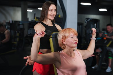 Photo of Senior woman training with dumbbells supervised by professional trainer in gym