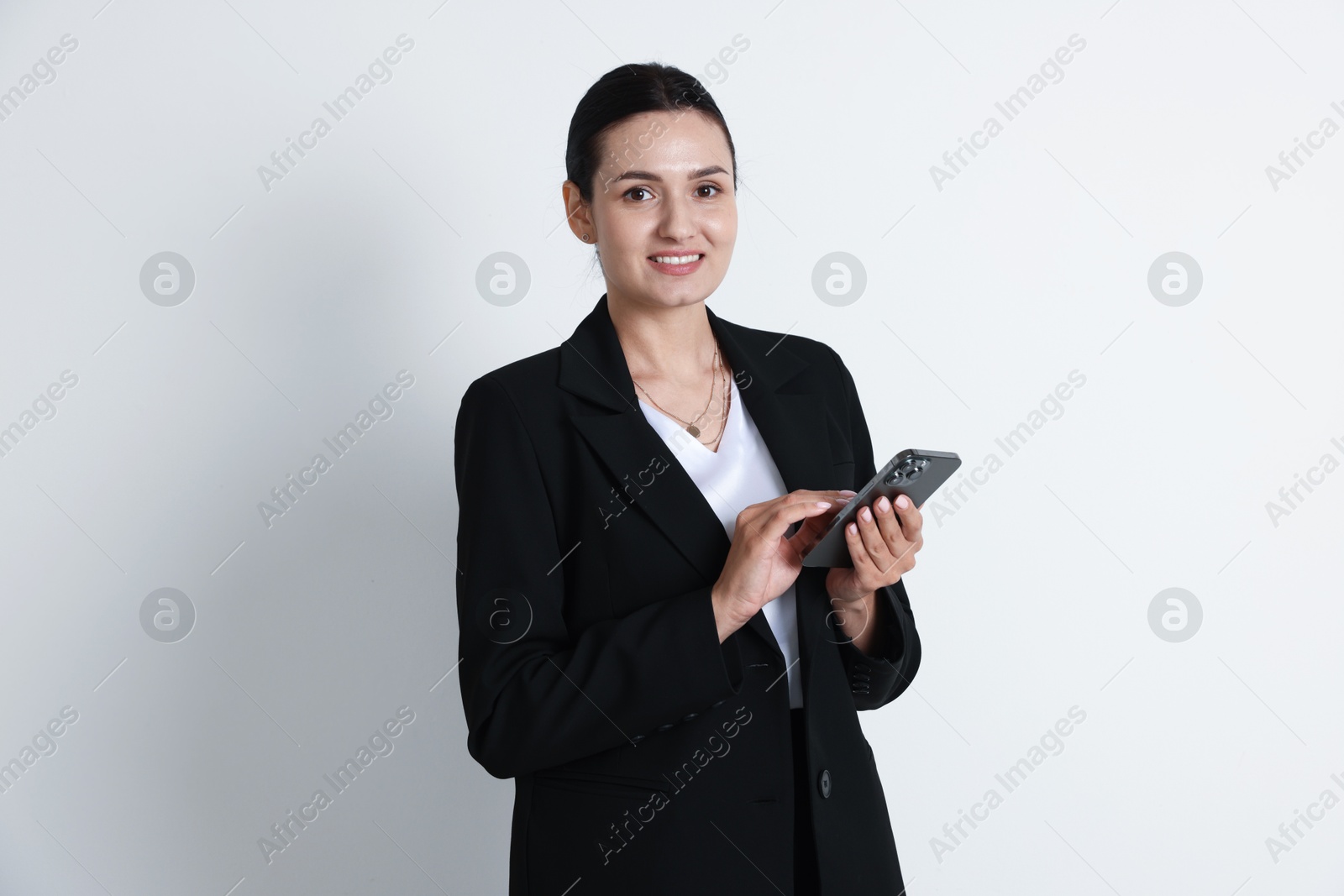 Confident business woman in suit with smartphone on light background Photo of Confident business woman in suit with smartphone on light background