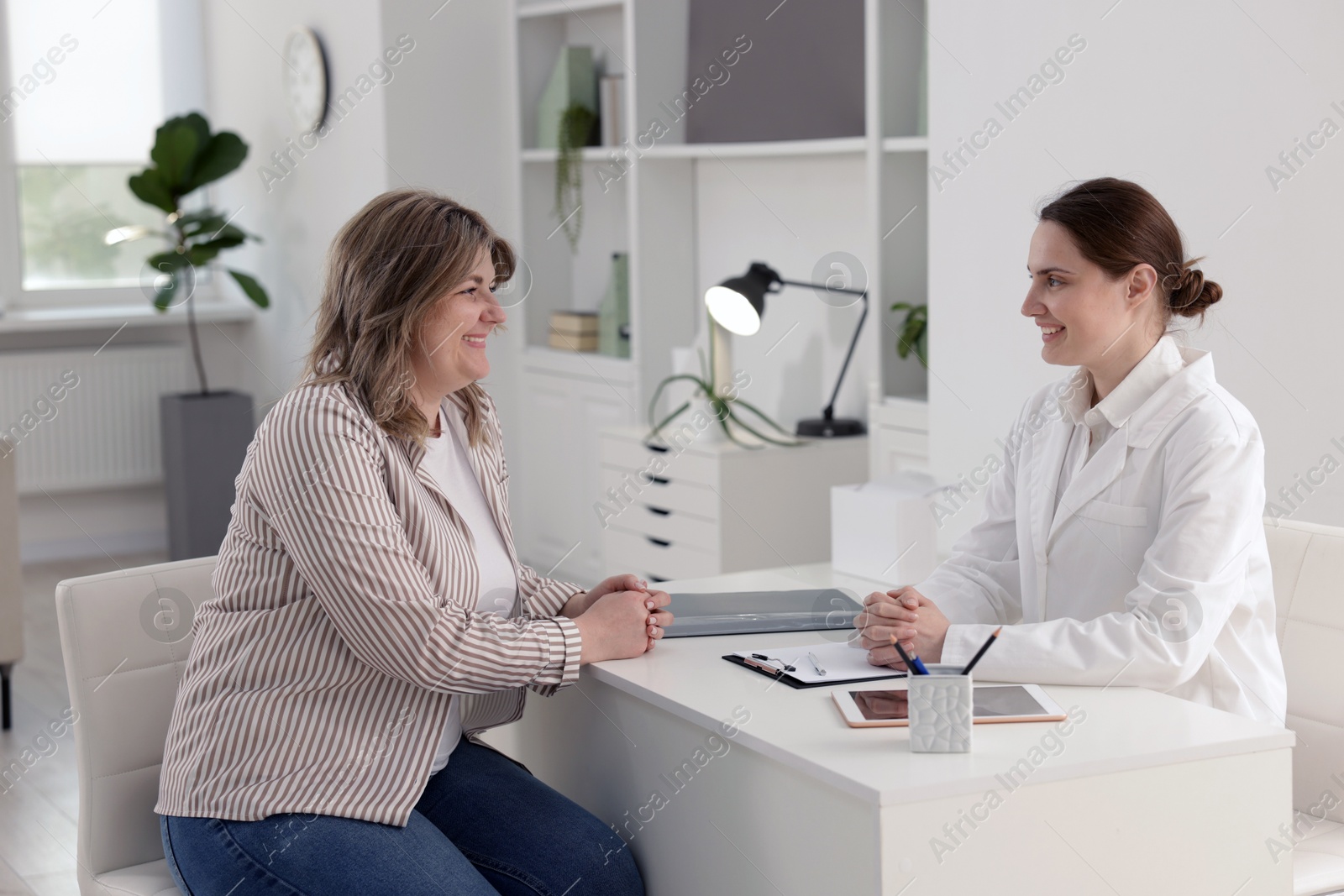 Weight loss. Nutritionist consulting overweight woman at white desk in clinic Photo of Weight loss. Nutritionist consulting overweight woman at white desk in clinic
