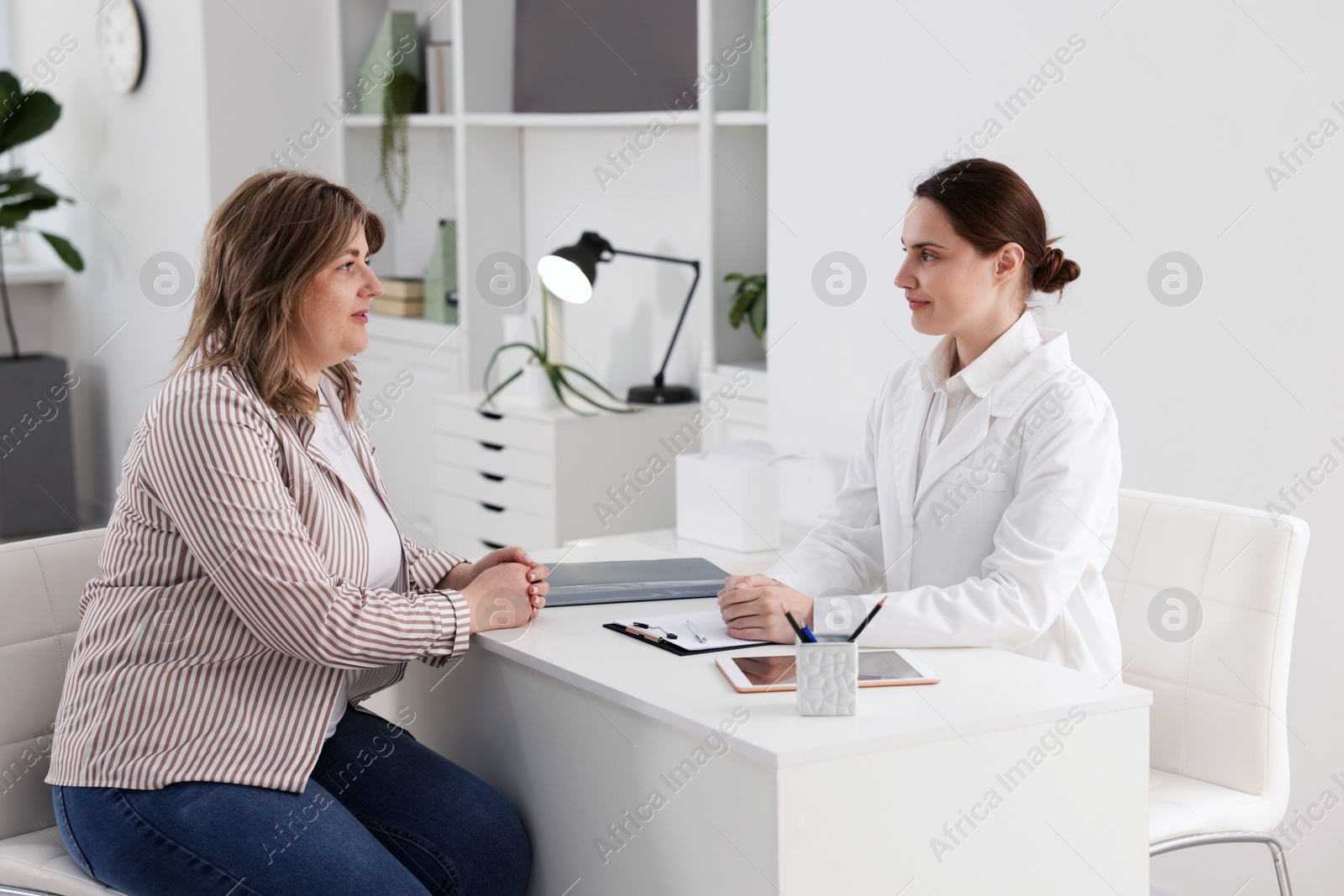 Weight loss. Nutritionist consulting overweight woman at white desk in clinic Photo of Weight loss. Nutritionist consulting overweight woman at white desk in clinic