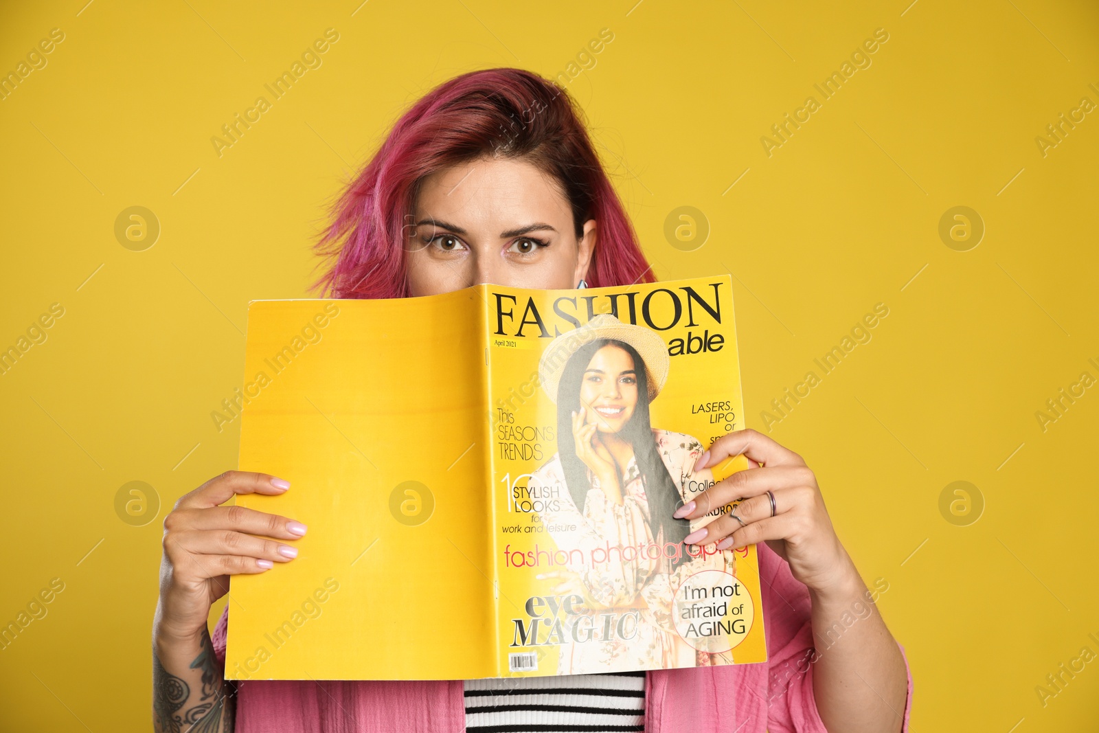 Beautiful woman with pink dyed hair holding fashion magazine on yellow background Photo of Beautiful woman with pink dyed hair holding fashion magazine on yellow background