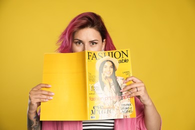 Photo of Beautiful woman with pink dyed hair holding fashion magazine on yellow background