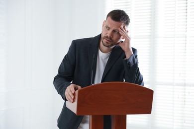 Photo of Fear of public speaking. Nervous man with microphone at lectern indoors