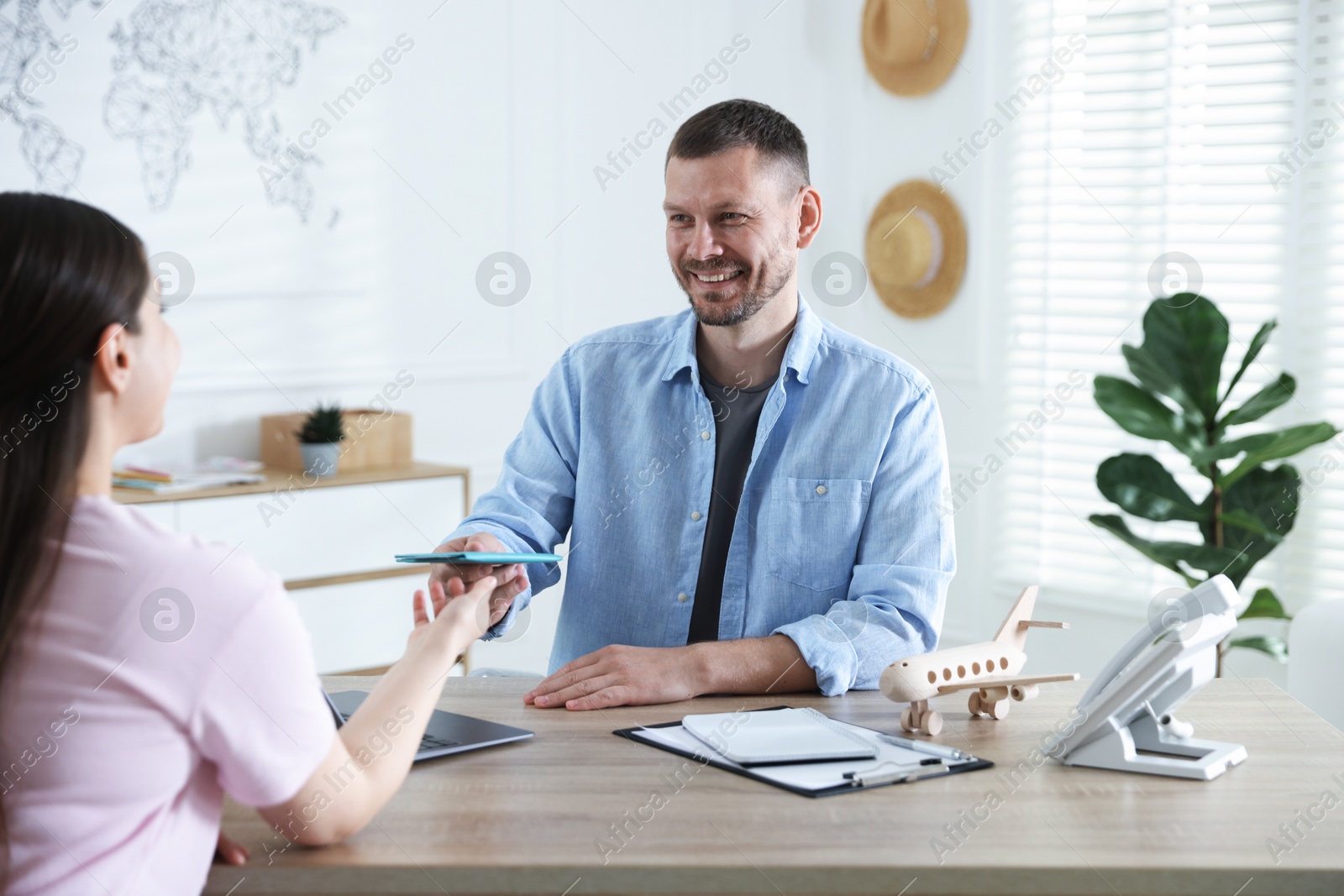 Travel agent giving passport with ticket to woman at wooden table in office Photo of Travel agent giving passport with ticket to woman at wooden table in office
