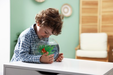 Photo of Cute little boy looking at gold fish in aquarium at white table indoors, space for text