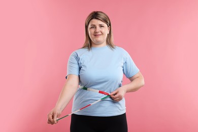 Photo of Weight loss. Plus size woman measuring waist with tape on pink background