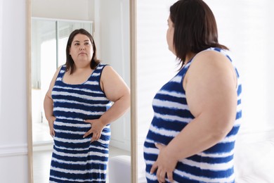 Photo of Overweight woman looking at herself in mirror indoors