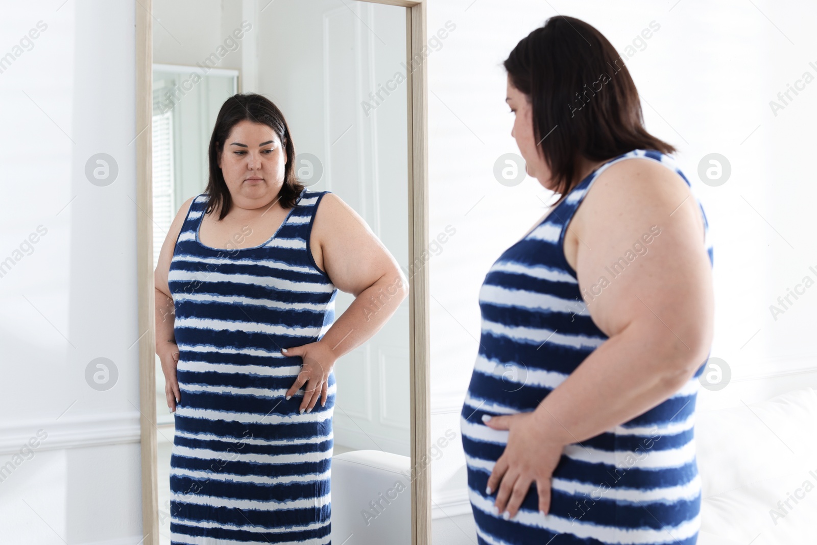 Overweight woman looking at herself in mirror indoors Photo of Overweight woman looking at herself in mirror indoors