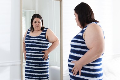 Photo of Overweight woman looking at herself in mirror indoors
