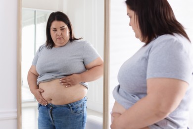 Photo of Woman with excessive belly fat near mirror indoors. Overweight problem