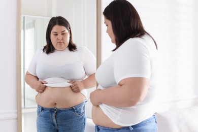Photo of Woman with excessive belly fat near mirror indoors. Overweight problem