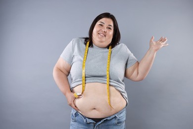 Photo of Overweight woman with measuring tape on grey background