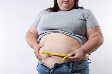 Photo of Overweight woman measuring her belly with tape on white background, closeup