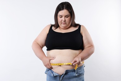 Photo of Overweight woman measuring her belly with tape on white background