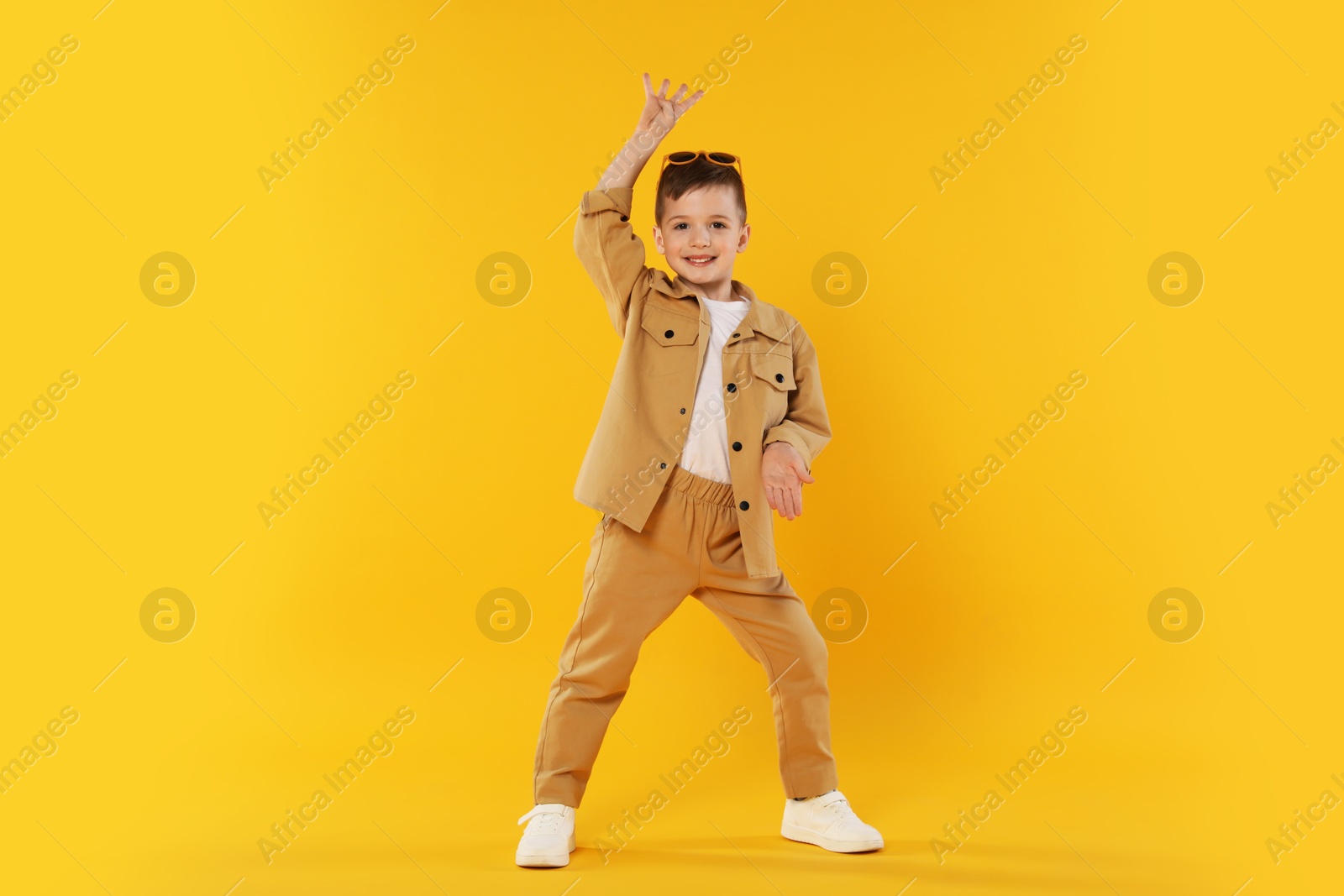 Happy little boy in sunglasses dancing on orange background Photo of Happy little boy in sunglasses dancing on orange background