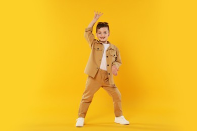 Photo of Happy little boy in sunglasses dancing on orange background