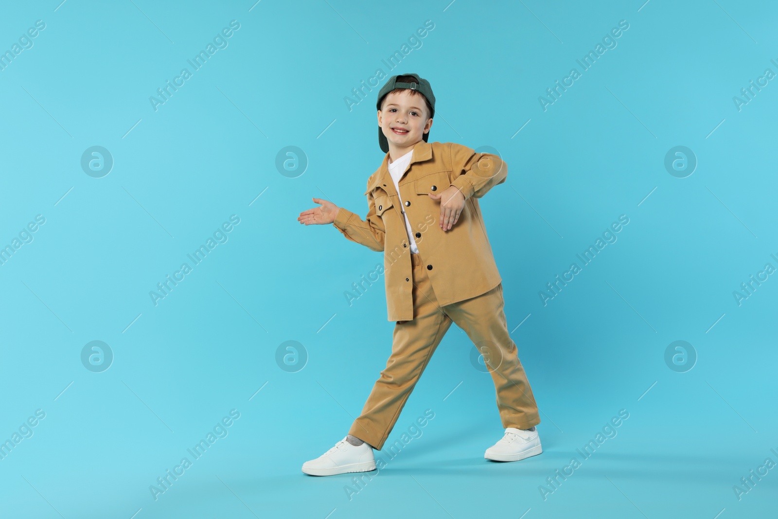 Happy little boy in baseball hat dancing on light blue background. Space for text Photo of Happy little boy in baseball hat dancing on light blue background. Space for text