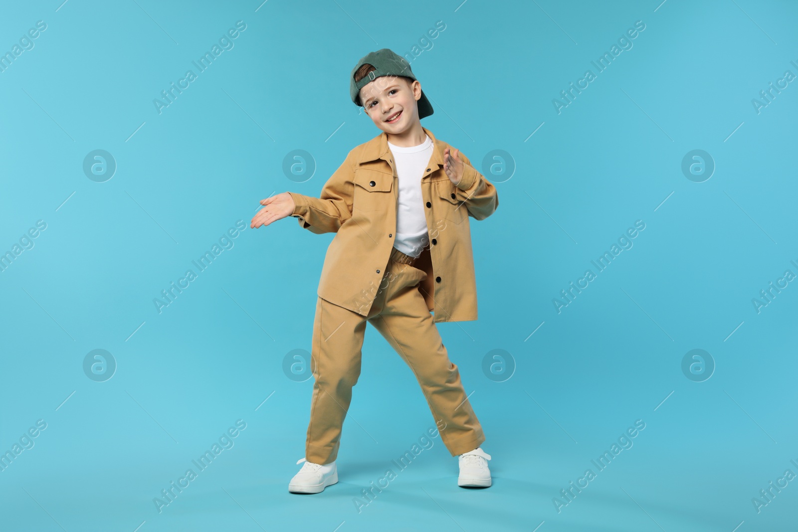 Photo of Happy little boy in baseball hat dancing on light blue background