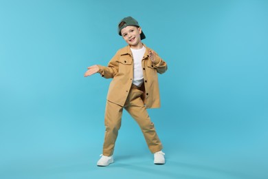 Photo of Happy little boy in baseball hat dancing on light blue background