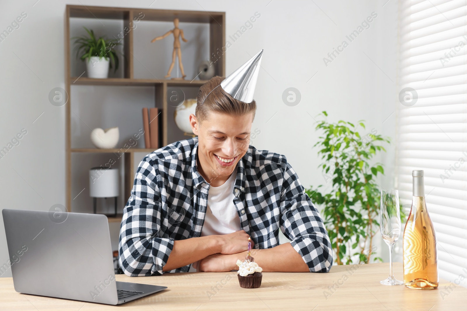 Birthday celebration. Man with cupcake and sparkling wine having video call via laptop at table indoors Photo of Birthday celebration. Man with cupcake and sparkling wine having video call via laptop at table indoors
