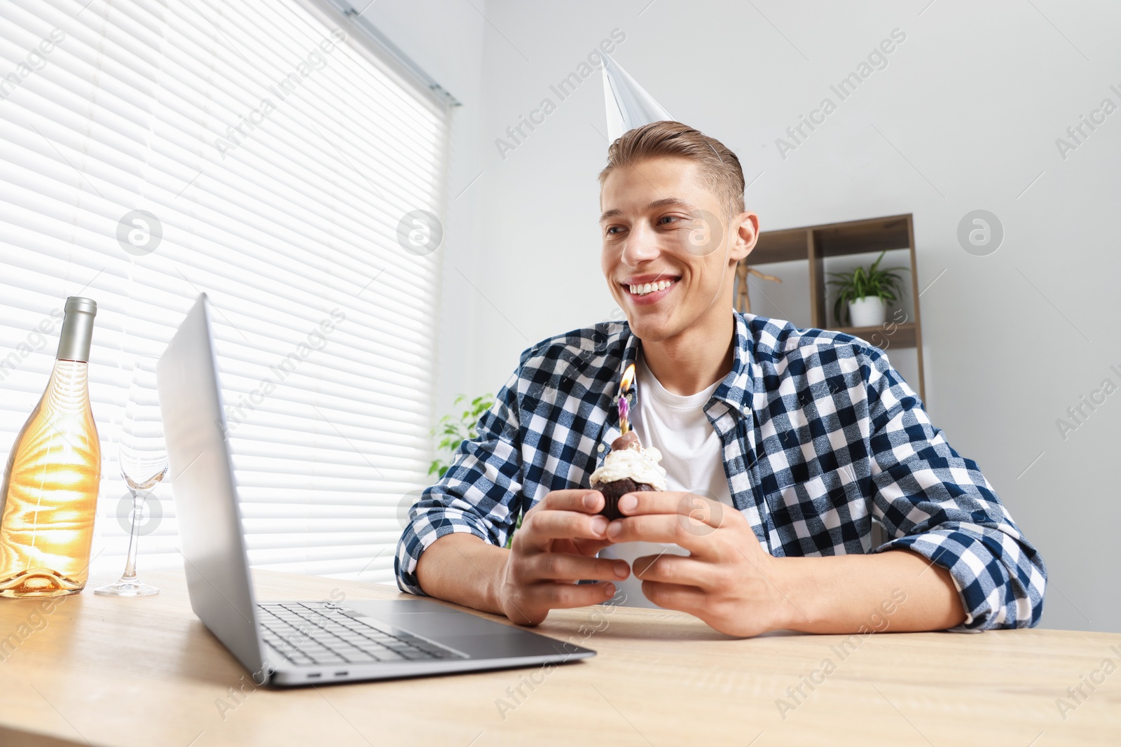Birthday celebration. Man with cupcake and sparkling wine having video call via laptop at table indoors, low angle view Photo of Birthday celebration. Man with cupcake and sparkling wine having video call via laptop at table indoors, low angle view
