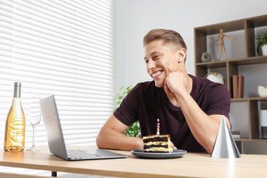 Photo of Birthday celebration. Man with cake and sparkling wine having video call via laptop at desk indoors, low angle view