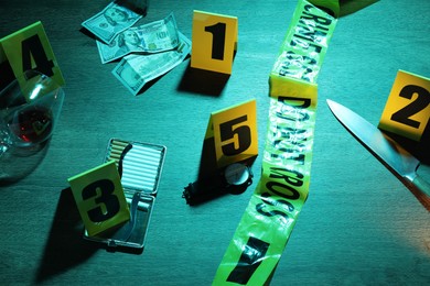 Photo of Forensic expertise. Crime scene with evidence, markers and police tape on wooden background, closeup. Color toned effect