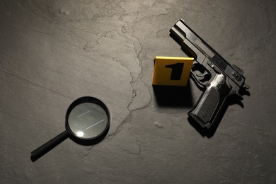 Photo of Forensic expertise. Crime scene with gun and magnifying glass on grey background, flat lay