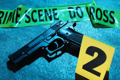 Photo of Forensic expertise. Crime scene tape and gun on blue background, closeup. Color toned effect