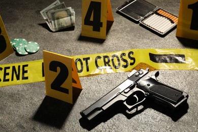 Photo of Forensic expertise. Crime scene with evidence, markers and police tape on grey background, closeup