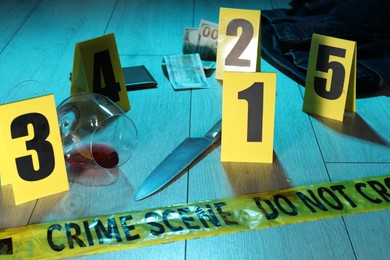 Photo of Forensic expertise. Crime scene with evidence, markers and police tape on floor, closeup. Color toned effect