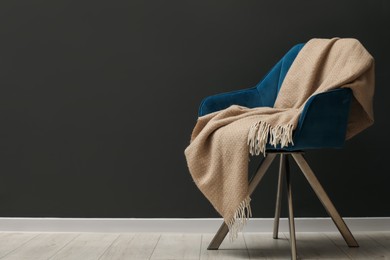 Photo of Comfortable armchair with beige woolen blanket near gray wall indoors, space for text