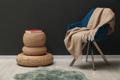 Photo of Comfortable armchair with beige woolen blanket and book near gray wall indoors