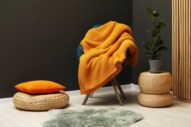Photo of Comfortable armchair with orange woolen blanket, houseplant and pillow indoors