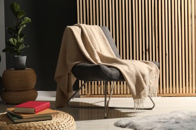 Photo of Comfortable armchair with woolen blanket, houseplant and books indoors