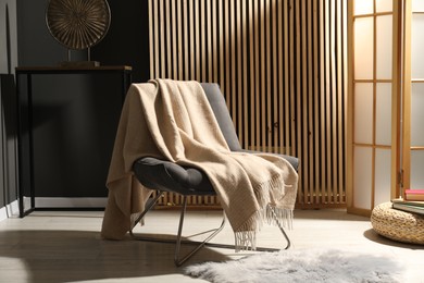 Photo of Comfortable armchair with woolen blanket in room