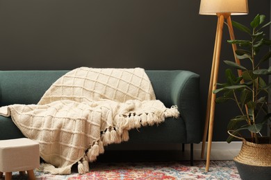 Photo of Beige woolen blanket on sofa, lamp, houseplant and ottoman indoors