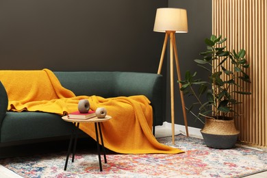Photo of Comfortable sofa with orange woolen blanket, book and decor on wooden table indoors