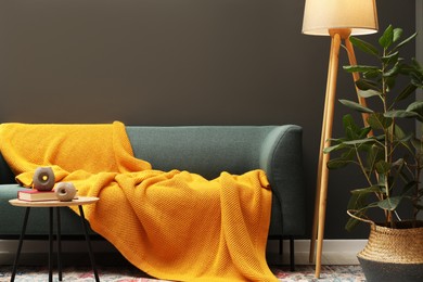 Photo of Comfortable sofa with orange woolen blanket, book and decor on wooden table indoors