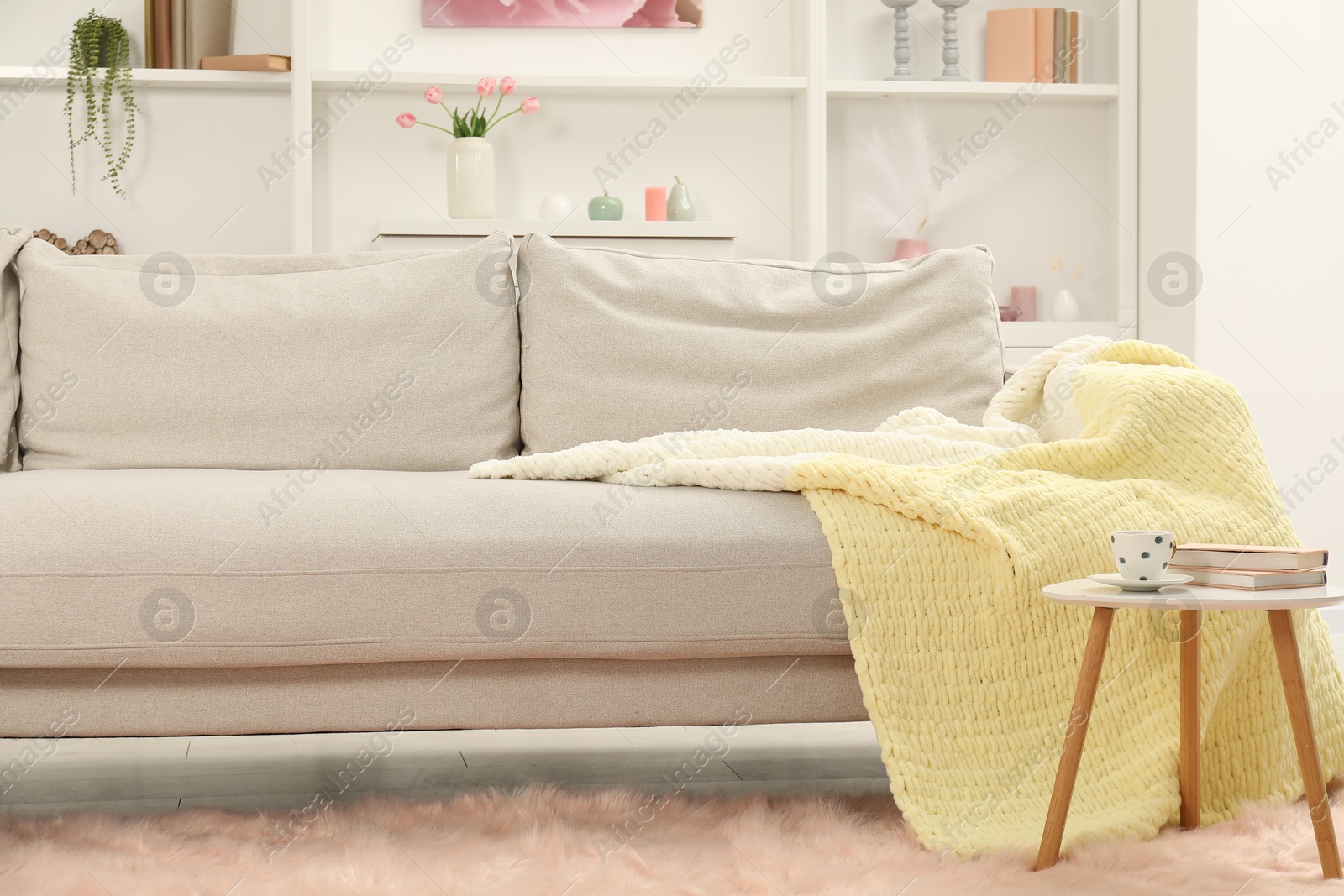 Comfortable sofa with woolen blanket, books and cup on side table indoors Photo of Comfortable sofa with woolen blanket, books and cup on side table indoors