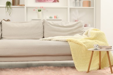 Photo of Comfortable sofa with woolen blanket, books and cup on side table indoors
