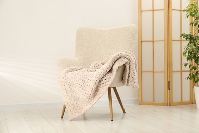 Photo of Comfortable armchair with woolen blanket in room
