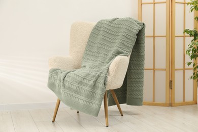 Photo of Comfortable armchair with green woolen blanket indoors